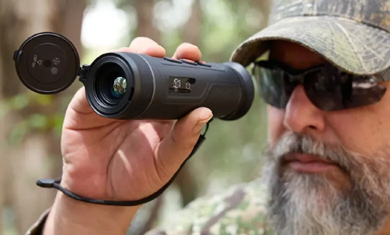 Man in camo hat uses a handheld thermal monocular for observation.