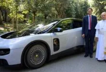 Pope Francis stands next to a man and a silver Ferrari Purosangue.