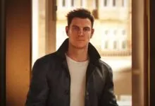 Man in leather jacket and earbuds stands in doorway.