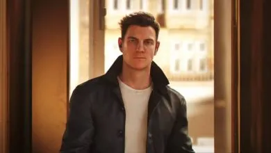 Man in leather jacket and earbuds stands in doorway.