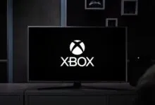 Xbox logo displayed on a large screen TV in a modern living room.