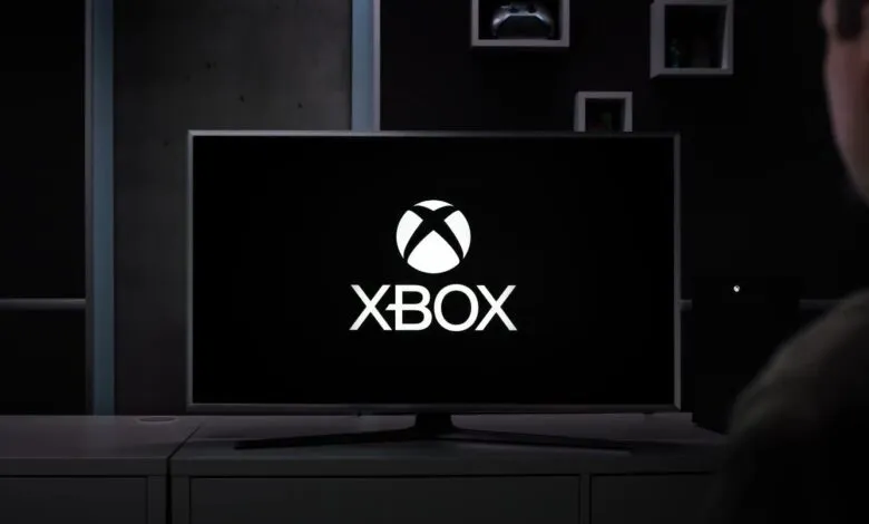 Xbox logo displayed on a large screen TV in a modern living room.