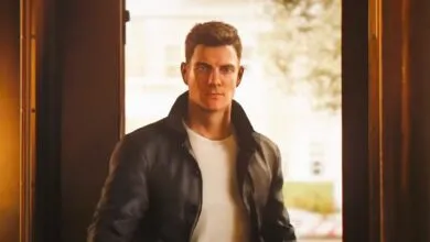 Man in leather jacket stands in doorway, looking forward.