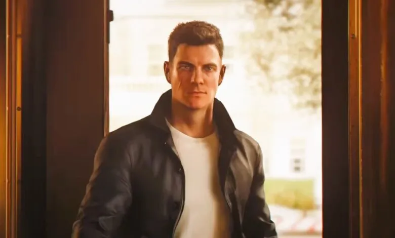 Man in leather jacket stands in doorway, looking forward.