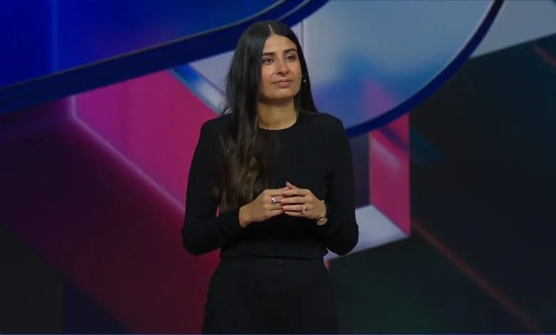Woman with long dark hair stands on stage in front of colorful backdrop.