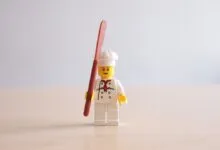 Lego chef minifigure stands holding a spatula against a plain background.