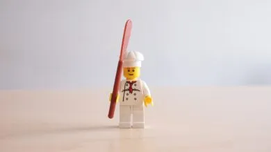 Lego chef minifigure stands holding a spatula against a plain background.
