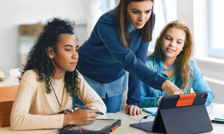 Three young women collaborate on a tablet device at a desk.