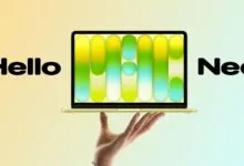 Laptop displaying colorful graphic held by a hand against a gradient background.