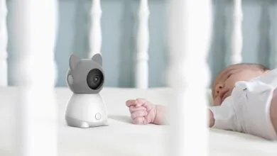 Baby monitor shaped like a cat next to a sleeping infant in a crib.