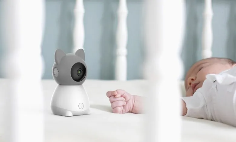 Baby monitor shaped like a cat next to a sleeping infant in a crib.