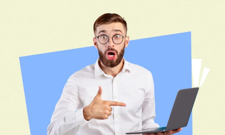 Surprised man with laptop points with open mouth, wearing glasses.