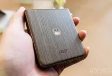 Hand holding a Motorola Razr phone with a wood-grain finish.