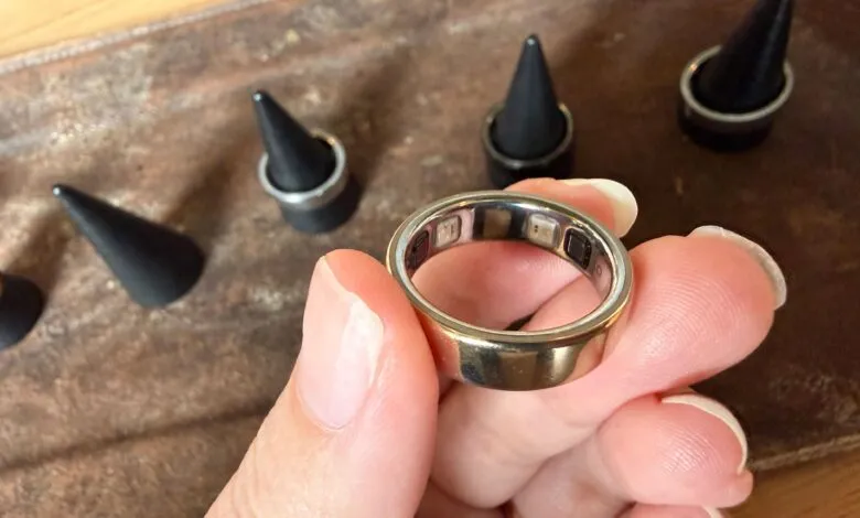 Hand holding gold Oura Ring with sensors visible inside.