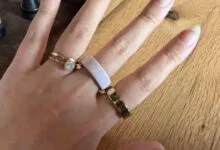 Hand wearing rose gold engagement ring and Oura ring on wooden surface.