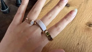 Hand wearing rose gold engagement ring and Oura ring on wooden surface.