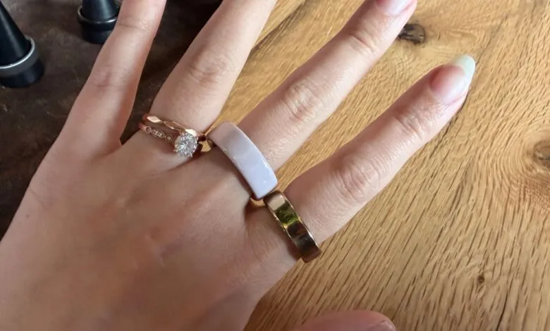 Hand wearing rose gold engagement ring and Oura ring on wooden surface.