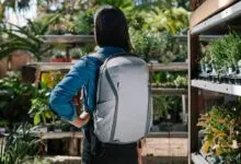 Person wearing a gray backpack in a plant nursery, back view.
