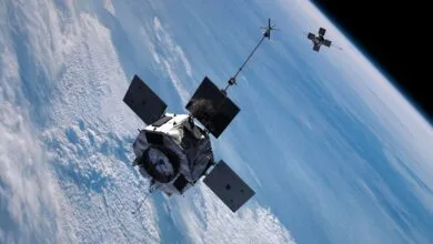 Two satellites orbit Earth, with clouds and blue sky visible below.