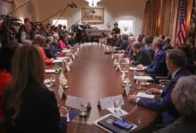 Oval Office meeting with long table, attendees, and press cameras.