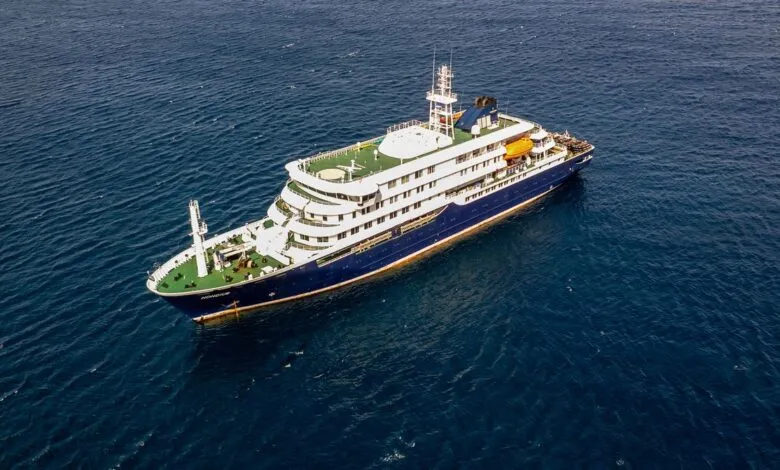 Aerial view of a blue and white expedition cruise ship sailing on the ocean.
