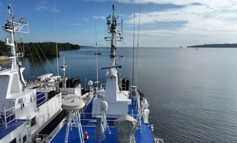 View from ship deck with white structures, antennas, and ocean backdrop.