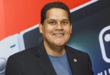 Reggie Fils-Aimé smiles in front of Nintendo Switch backdrop.