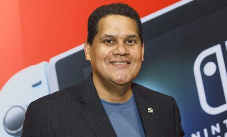 Reggie Fils-Aimé smiles in front of Nintendo Switch backdrop.