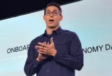 RJ Scaringe, Rivian CEO, presents onstage with hands clasped and wearing glasses.