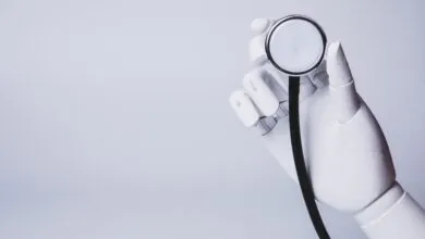 White robotic hand holding a stethoscope against a light gray background.