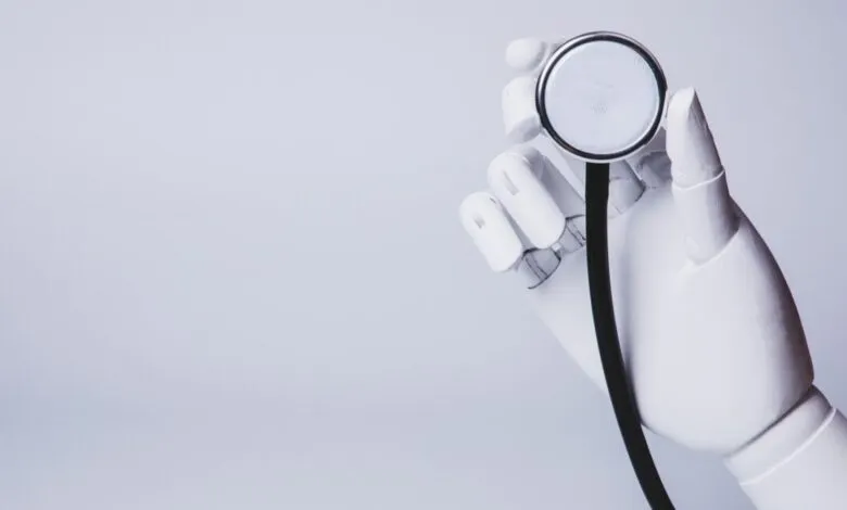 White robotic hand holding a stethoscope against a light gray background.