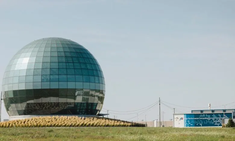Large glass dome building with blue panels, surrounded by field.
