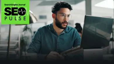 Man with glasses intently working on a laptop in a bright office setting.