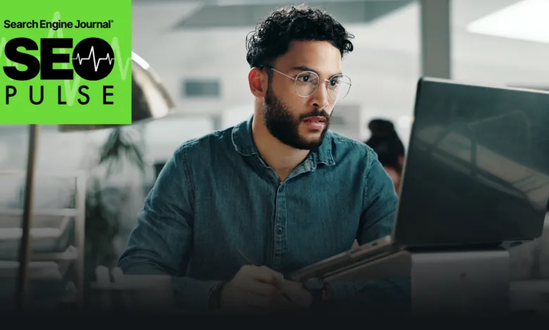 Man with glasses intently working on a laptop in a bright office setting.