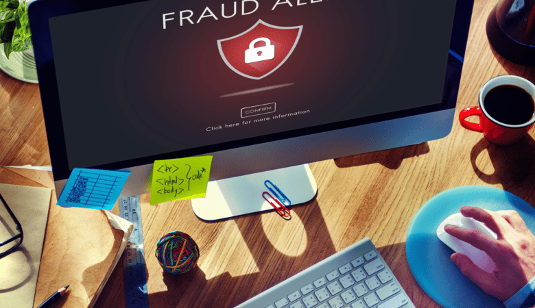 Computer screen displays 'Fraud Alert' with padlock icon, keyboard, and coffee.