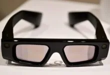 Black augmented reality glasses with reflective lenses on a white surface.