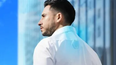 Man in white shirt with wearable device on back of neck, city backdrop.