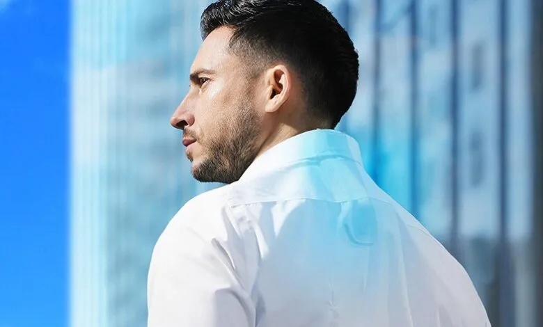 Man in white shirt with wearable device on back of neck, city backdrop.