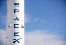Close-up of a SpaceX rocket with blue lettering against a clear blue sky.