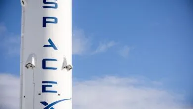 Close-up of a SpaceX rocket with blue lettering against a clear blue sky.