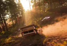 Rally cars race through a sunlit forest on a dirt track, kicking up dust.