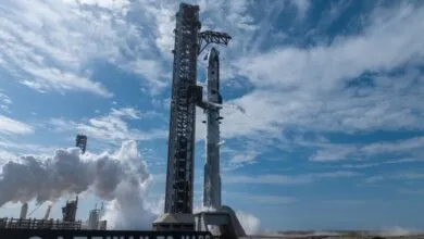 SpaceX Starship rocket on launchpad with vapor trails against blue sky.