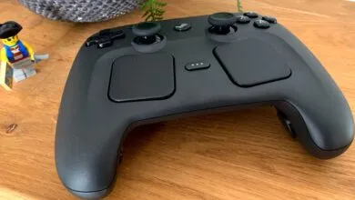 Black Steam Controller sits on a wooden surface next to a Lego pirate.
