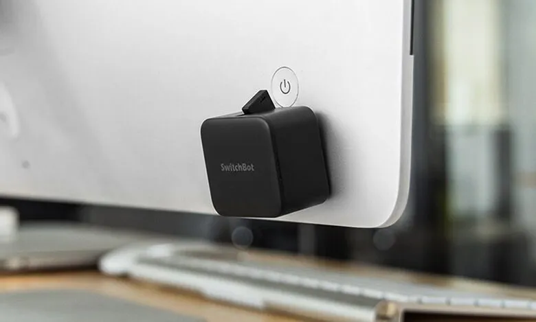 SwitchBot attached to a monitor power button for smart home automation.