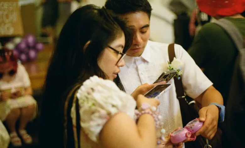 Couple at wedding playing with phones and a pink Tamagotchi toy.
