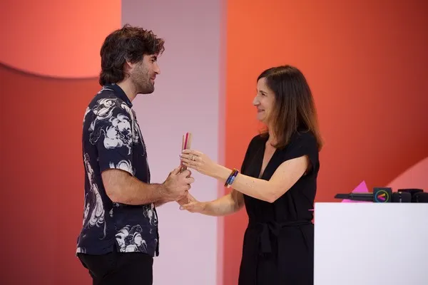 Man and woman exchanging an award on a colorful stage.