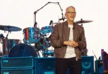 Tim Cook stands on stage near a drum set and amplifiers.