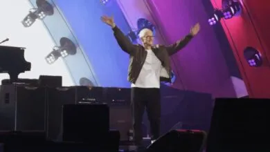 Tim Cook on stage with arms raised, lit by colorful stage lights.