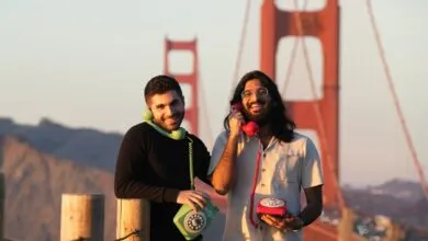 Two smiling men pose with rotary phones in front of Golden Gate Bridge.