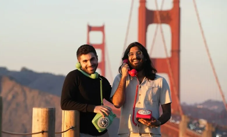 Two smiling men pose with rotary phones in front of Golden Gate Bridge.